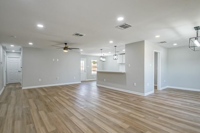 unfurnished living room with ceiling fan with notable chandelier and light hardwood / wood-style floors