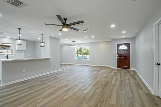 unfurnished living room featuring ceiling fan with notable chandelier and light hardwood / wood-style floors