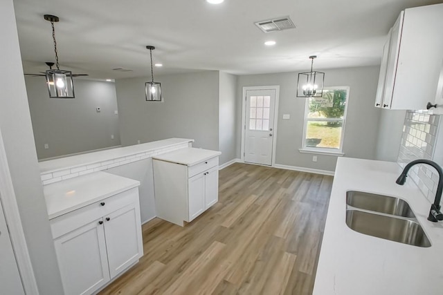 kitchen featuring ceiling fan with notable chandelier, backsplash, light hardwood / wood-style floors, sink, and white cabinetry