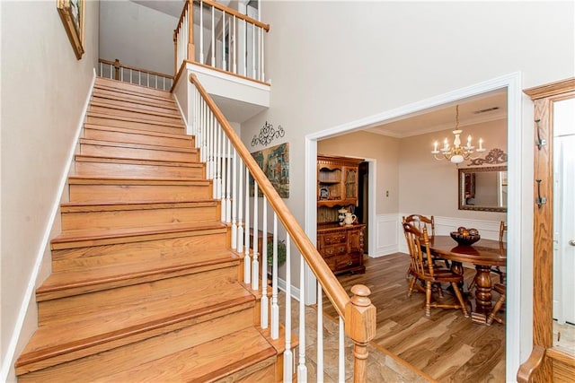 staircase with wood-type flooring, ornamental molding, a high ceiling, and an inviting chandelier