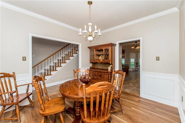 dining room featuring light hardwood / wood-style floors, ornamental molding, a textured ceiling, and an inviting chandelier