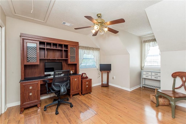 home office with a textured ceiling, light wood-type flooring, vaulted ceiling, and ceiling fan