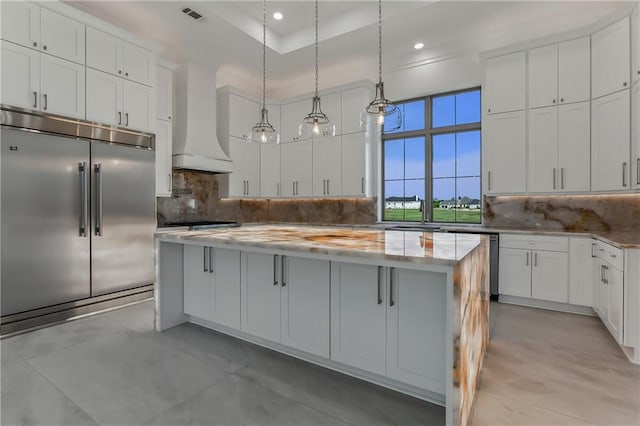 kitchen featuring custom range hood, a center island, stainless steel appliances, decorative backsplash, and white cabinetry