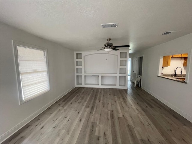 unfurnished living room with hardwood / wood-style floors, ceiling fan, sink, and a textured ceiling