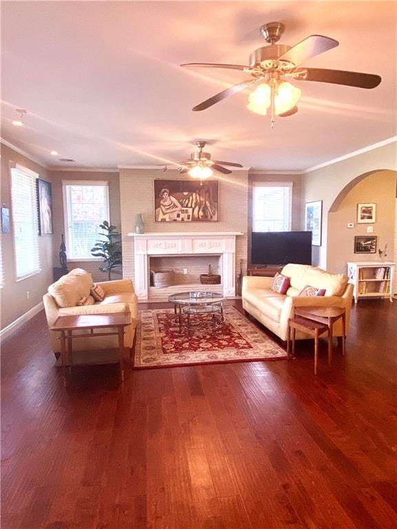 living area featuring arched walkways, a fireplace, wood finished floors, baseboards, and ornamental molding