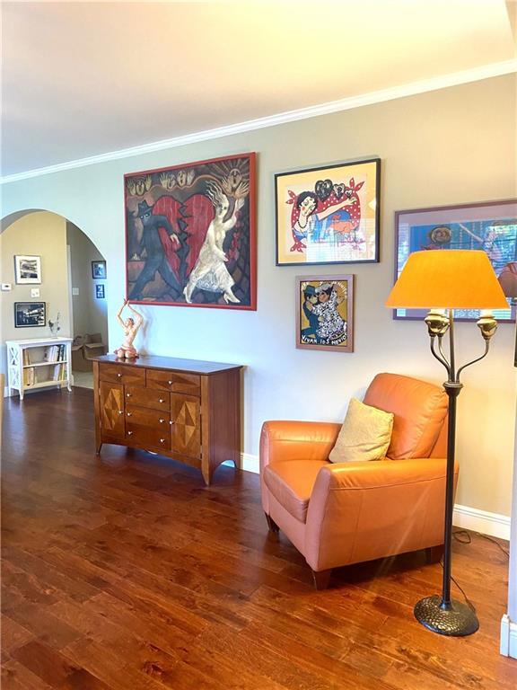 sitting room with baseboards, arched walkways, wood finished floors, and ornamental molding