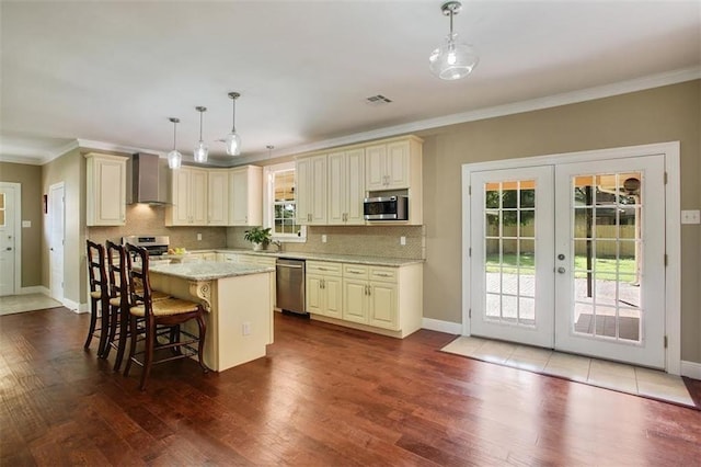 kitchen with cream cabinets, stainless steel appliances, french doors, a center island, and wall chimney exhaust hood