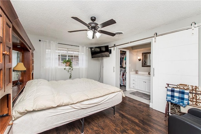 bedroom with a textured ceiling, dark hardwood / wood-style flooring, ceiling fan, ensuite bathroom, and a barn door