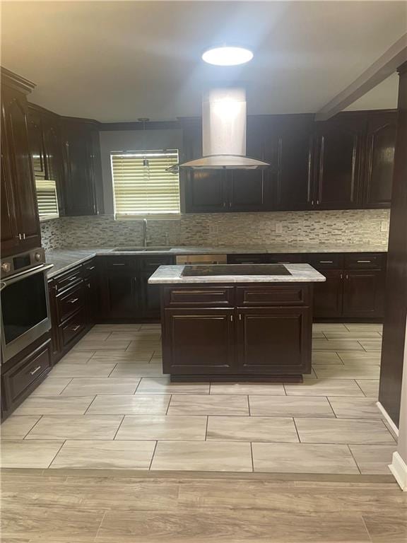 kitchen with light tile patterned floors, tasteful backsplash, island exhaust hood, sink, and stainless steel oven