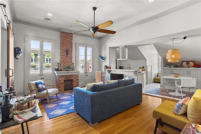 living room featuring light wood-type flooring, ceiling fan, a fireplace, and crown molding