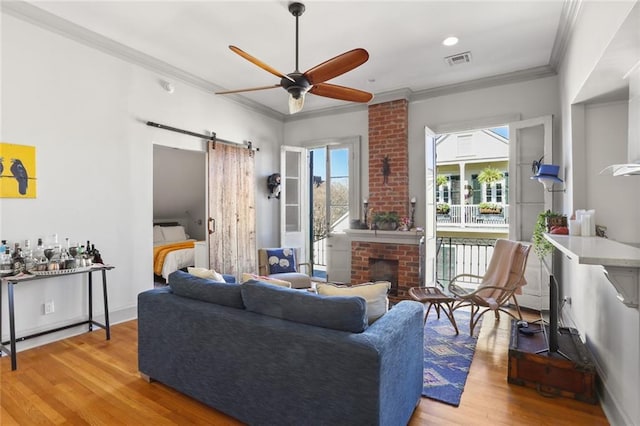 living room featuring light wood-type flooring, a fireplace, a barn door, ornamental molding, and ceiling fan