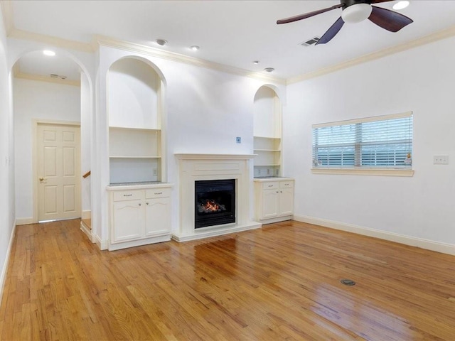 unfurnished living room featuring built in features, ceiling fan, ornamental molding, and light wood-type flooring