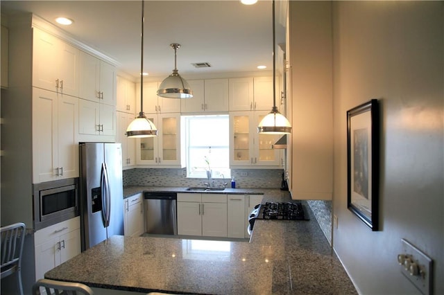 kitchen with pendant lighting, sink, white cabinets, stainless steel appliances, and dark stone countertops