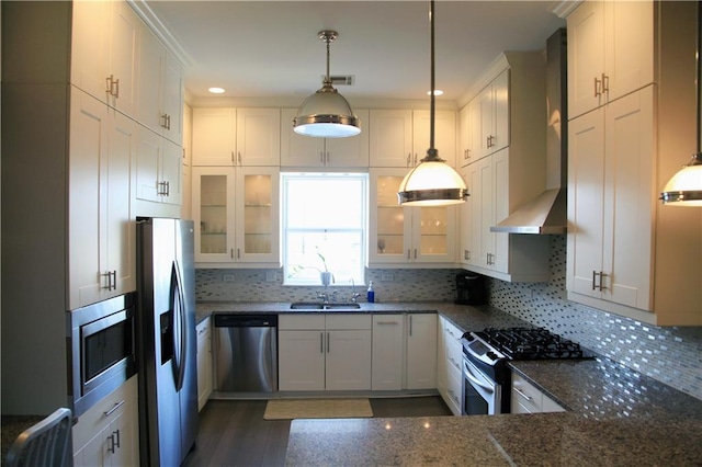 kitchen with pendant lighting, white cabinetry, wall chimney range hood, backsplash, and appliances with stainless steel finishes