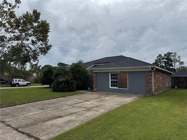 view of side of property with concrete driveway, brick siding, a yard, and a shingled roof