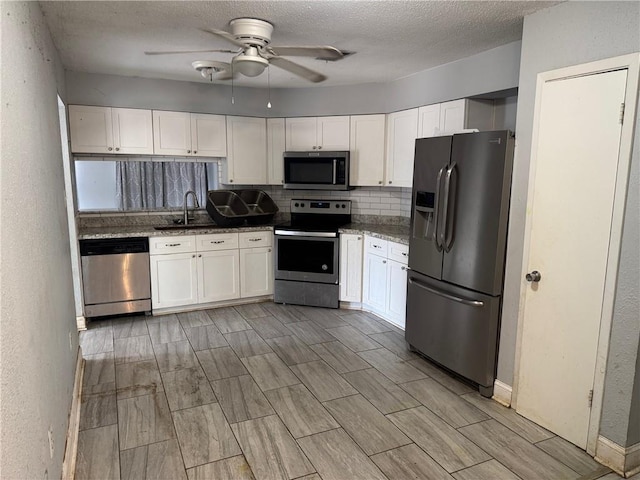 kitchen featuring white cabinets, stainless steel appliances, a ceiling fan, a sink, and decorative backsplash