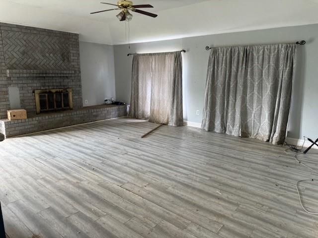 unfurnished living room featuring wood finished floors, a brick fireplace, and ceiling fan