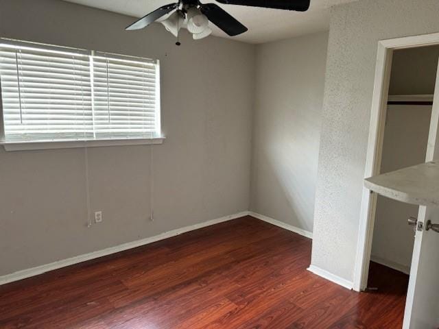 unfurnished bedroom featuring ceiling fan, a closet, dark wood-type flooring, and a spacious closet