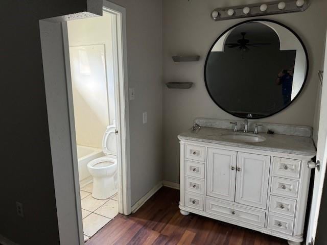full bathroom with toilet, baseboards, a ceiling fan, wood finished floors, and vanity