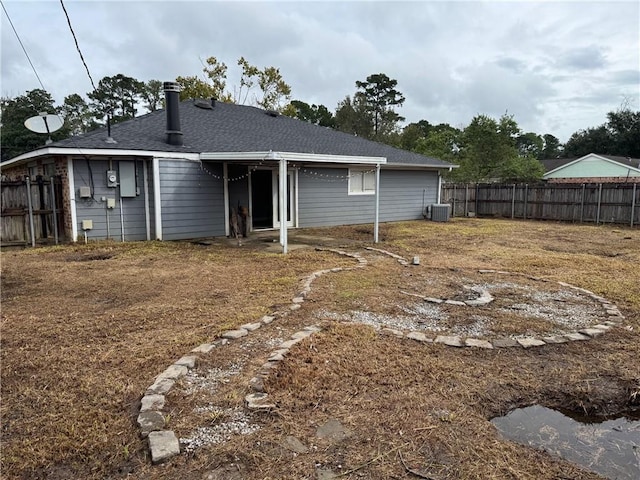 rear view of property featuring fence, a shingled roof, and central AC