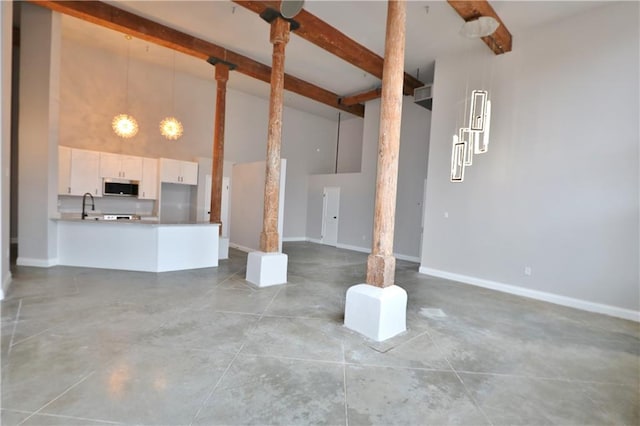 unfurnished living room featuring a towering ceiling, beamed ceiling, concrete floors, and sink