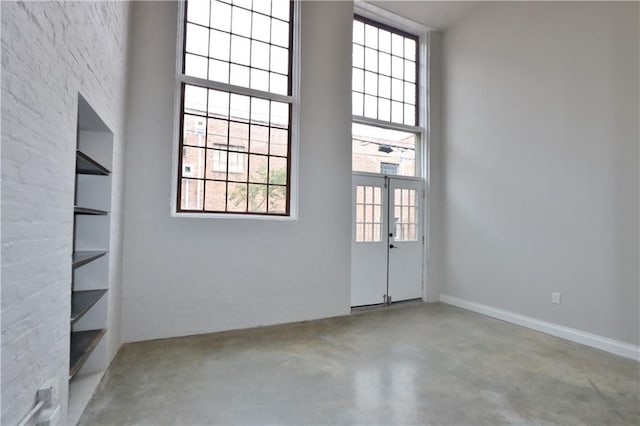 unfurnished room with built in features, french doors, concrete floors, and a towering ceiling