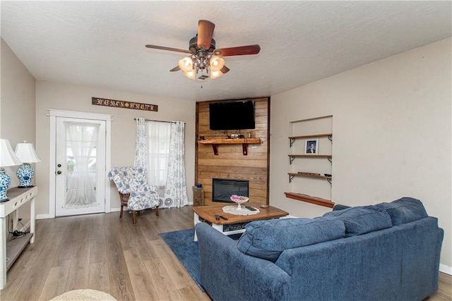 living room with a textured ceiling, ceiling fan, wood-type flooring, and a fireplace