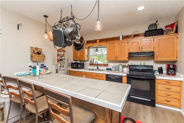 kitchen with black appliances, sink, hanging light fixtures, a breakfast bar, and light hardwood / wood-style floors