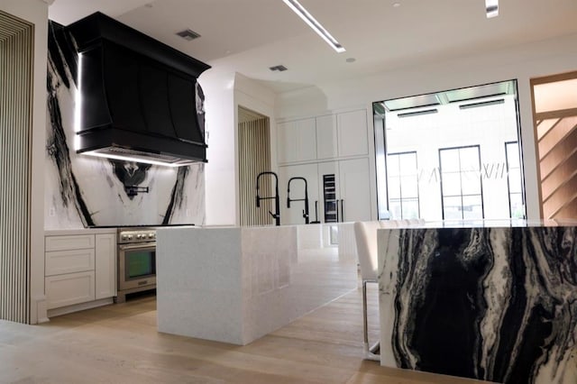 kitchen featuring stainless steel stove, light hardwood / wood-style flooring, light stone countertops, custom exhaust hood, and white cabinetry