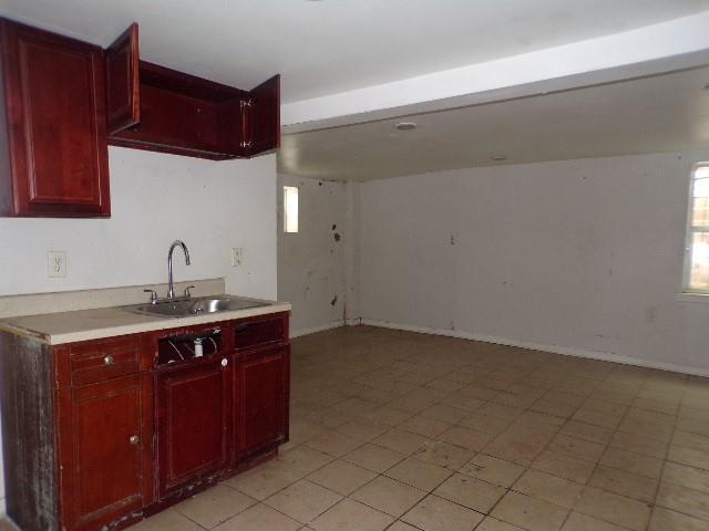 kitchen featuring a sink, baseboards, reddish brown cabinets, and light countertops