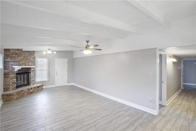 unfurnished living room featuring ceiling fan, beamed ceiling, a fireplace, and light hardwood / wood-style flooring