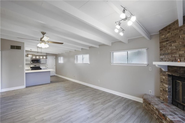 unfurnished living room with light hardwood / wood-style flooring, vaulted ceiling with beams, ceiling fan, and a fireplace