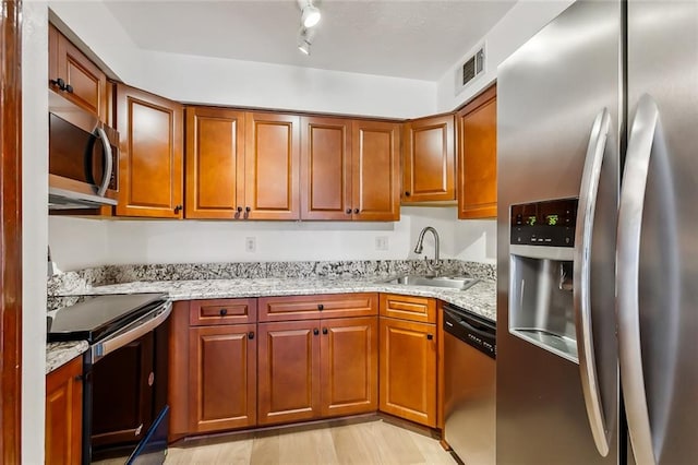 kitchen with light stone countertops, stainless steel appliances, sink, and light hardwood / wood-style floors