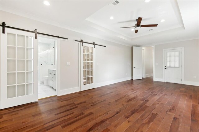 empty room with a barn door, hardwood / wood-style floors, ceiling fan, and a raised ceiling