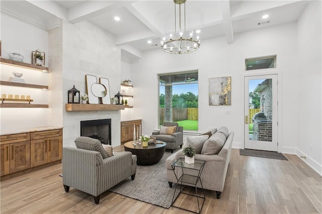 living room with an inviting chandelier, beamed ceiling, light hardwood / wood-style flooring, a large fireplace, and a towering ceiling