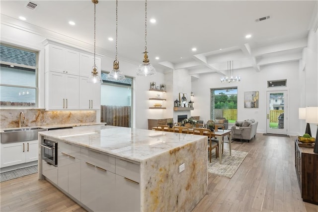 kitchen with coffered ceiling, a center island, sink, beam ceiling, and white cabinets