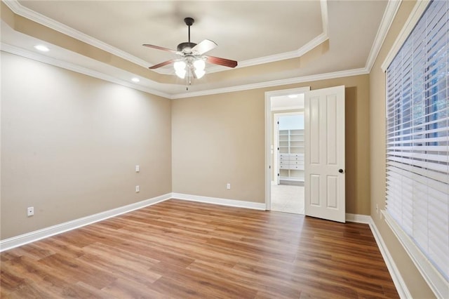 empty room with a raised ceiling, ornamental molding, hardwood / wood-style floors, and ceiling fan