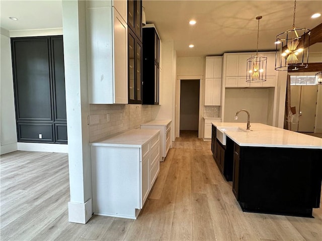 kitchen featuring an island with sink, decorative backsplash, light hardwood / wood-style flooring, and white cabinets