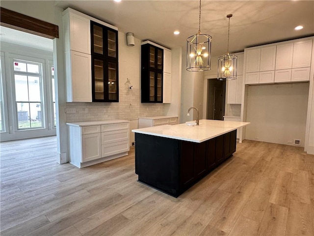 kitchen featuring a center island with sink, decorative light fixtures, backsplash, and light hardwood / wood-style flooring