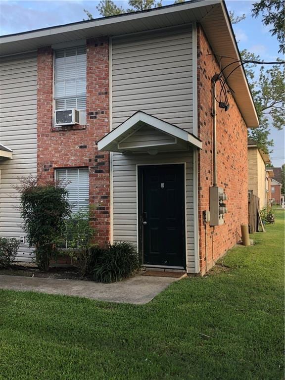 property entrance featuring cooling unit, a lawn, and brick siding