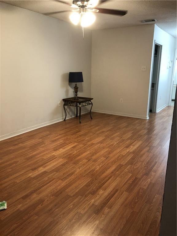 empty room featuring baseboards, dark wood-type flooring, visible vents, and a ceiling fan