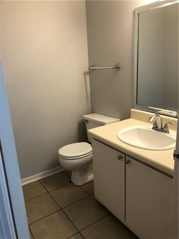 half bathroom featuring toilet, tile patterned flooring, baseboards, and vanity