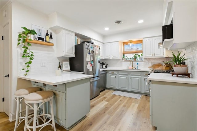 kitchen with a kitchen breakfast bar, stainless steel fridge, kitchen peninsula, sink, and light wood-type flooring