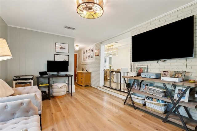 living room with brick wall, light hardwood / wood-style floors, a notable chandelier, and ornamental molding