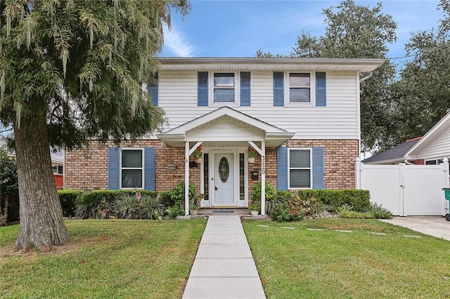 traditional home featuring brick siding, a front lawn, fence, and a gate