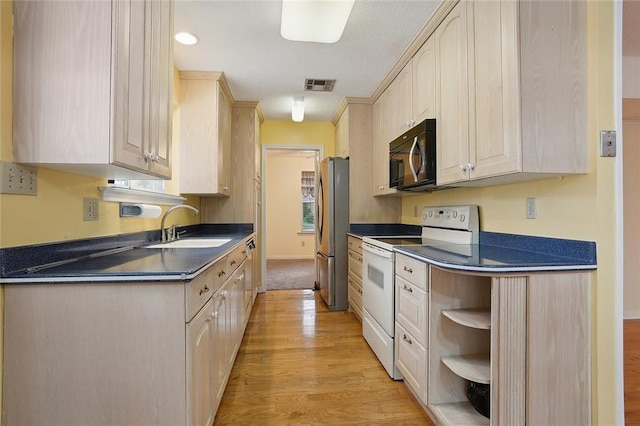 kitchen featuring a sink, freestanding refrigerator, light brown cabinetry, white range with electric cooktop, and dark countertops