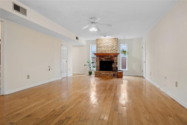 unfurnished living room featuring light wood finished floors, visible vents, a ceiling fan, a brick fireplace, and baseboards