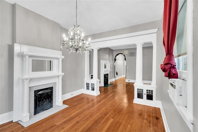 interior space featuring wood finished floors, a fireplace with flush hearth, decorative columns, and baseboards