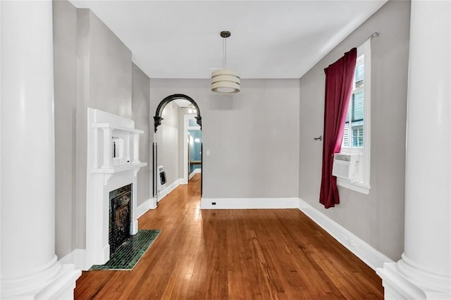 unfurnished dining area with ornate columns, a fireplace with flush hearth, cooling unit, baseboards, and hardwood / wood-style flooring