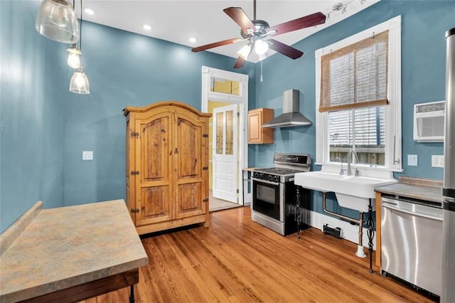 kitchen featuring ceiling fan, light wood-style floors, an AC wall unit, appliances with stainless steel finishes, and wall chimney range hood